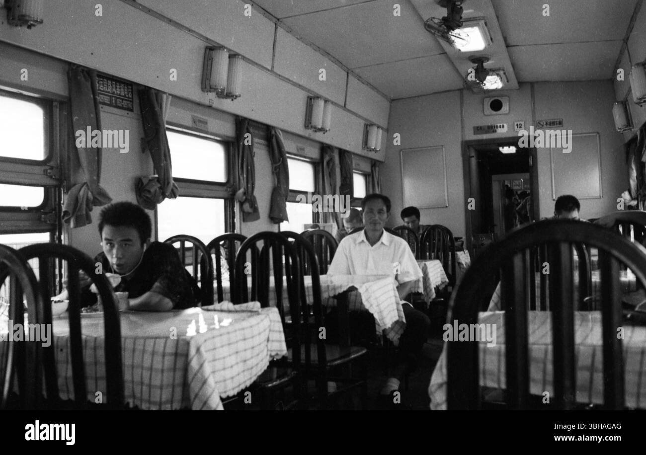 Passengers dine and rest in a Chinese train dining car amid checkered tablecloths and classic decor – a timeless scene of rail travel in 2000s China